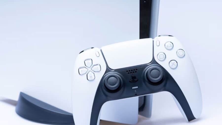 Primo piano di un controller DualSense bianco e nero appoggiato davanti a una PlayStation 5.