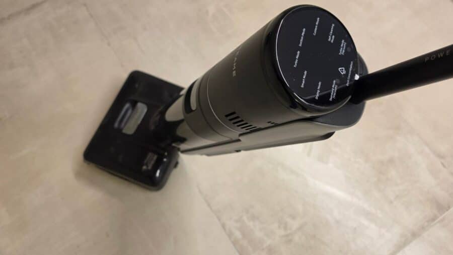 Vista ravvicinata della stazione di ricarica e autopulizia del Dreame H15 Mix sul pavimento, con modulo lavatappeti grigio agganciato lateralmente, tubo flessibile avvolto e bocchetta con spazzole inserita nell'apposito alloggiamento