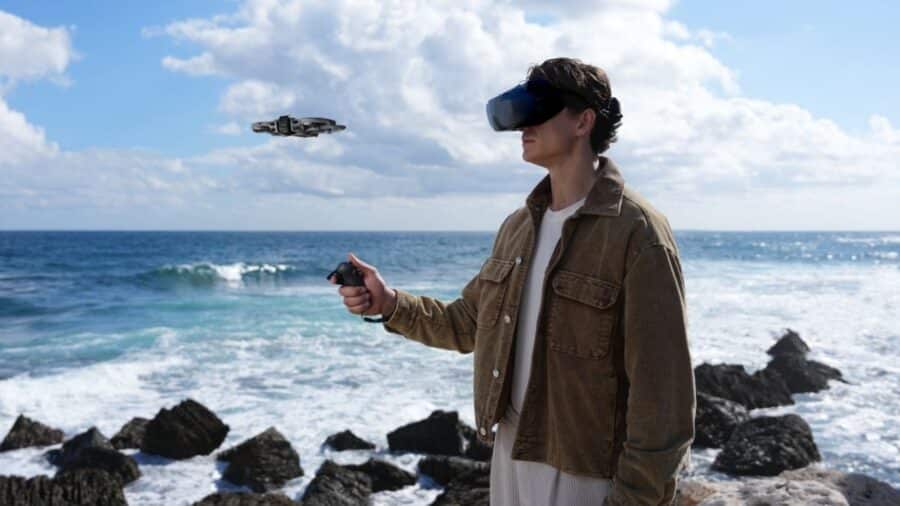Pilota con DJI Goggles e Motion Controller che vola con il DJI Avata 360 sullo sfondo di una costa rocciosa e mare