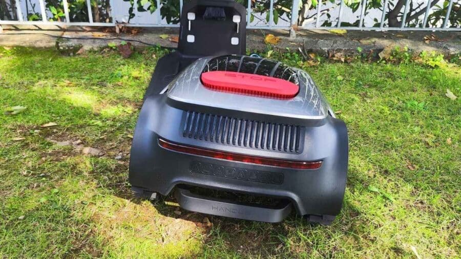 Vista posteriore del Dreame Roboticmower A2 con pulsante STOP rosso e stazione di ricarica sullo sfondo