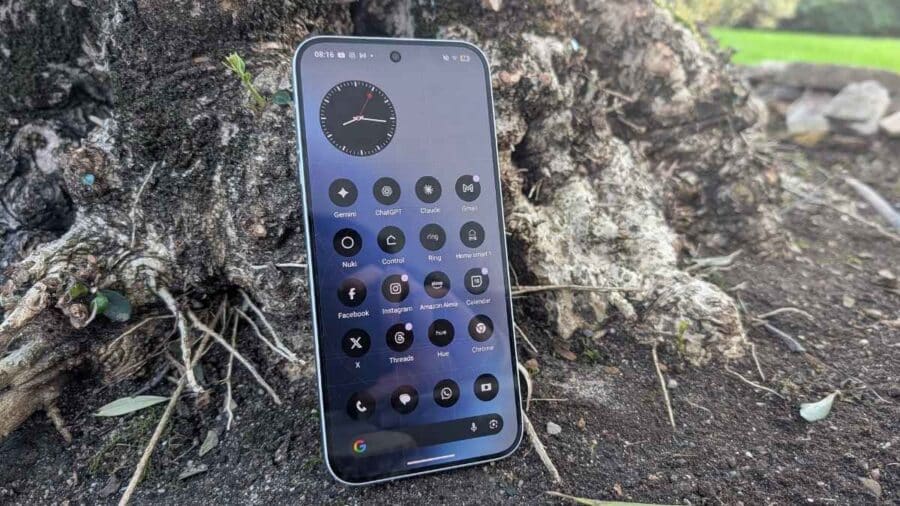 Nothing Phone (4a) Pro appoggiato su corteccia con schermo frontale acceso che mostra la home screen di Nothing OS 4.1 con widget orologio e icone circolari