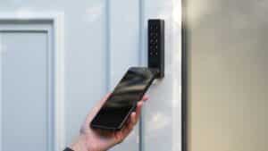 Nuki Keypad 2 NFC installato sul muro accanto a una porta bianca, con tastiera numerica sensore NFC e lettore di impronte