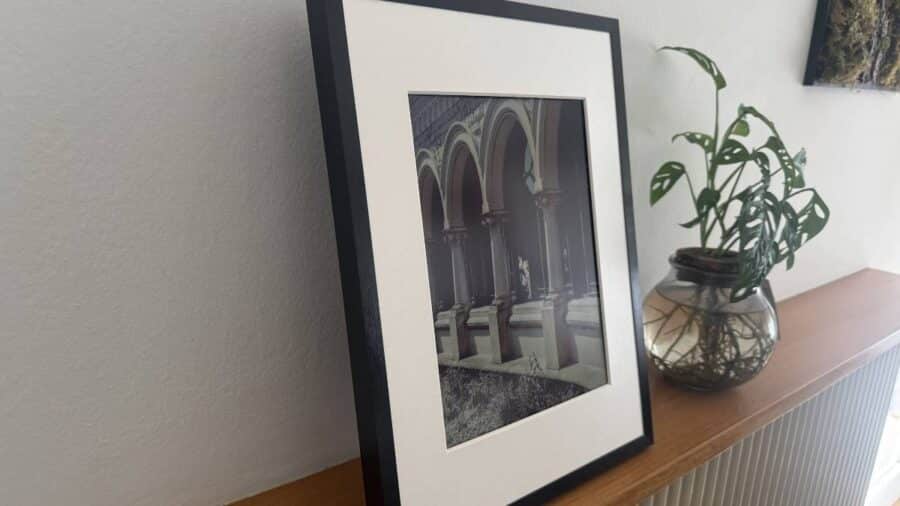 Vista laterale della cornice SwitchBot AI Art Frame con immagine architettonica, appoggiata su una mensola vicino a una pianta in vaso.