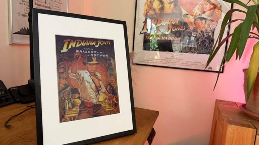 Una cornice SwitchBot AI Art Frame con un poster di Indiana Jones è posata su una scrivania, con altri poster cinematografici sullo sfondo.