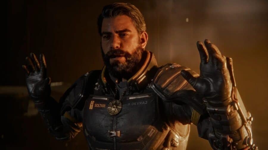 Primo piano di Arjun Devraj, protagonista di Saros, in armatura futuristica mentre alza le mani in una scena narrativa illuminata da toni caldi.