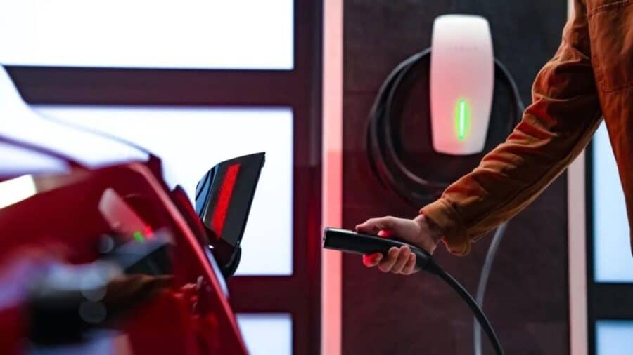 Una persona collega il cavo di ricarica a un’auto elettrica davanti a una wallbox domestica illuminata.