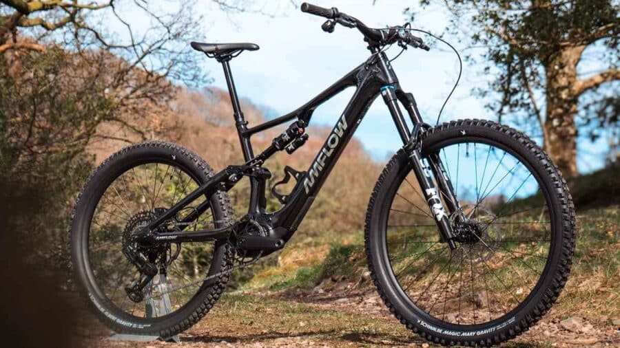 Una e-mountain bike Amflow nera è fotografata all’aperto su un sentiero, con sospensioni complete e telaio sportivo in evidenza.