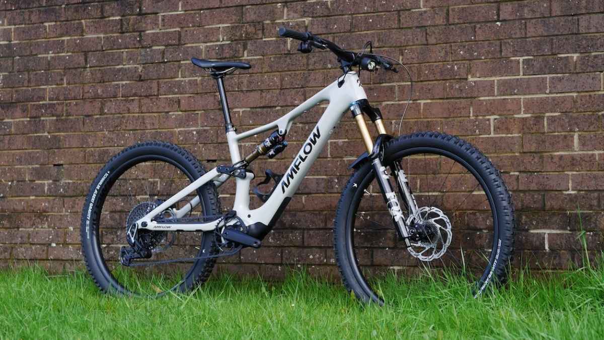 Una e-mountain bike Amflow chiara è appoggiata contro un muro di mattoni, con forcella ammortizzata e ruote tassellate in primo piano.