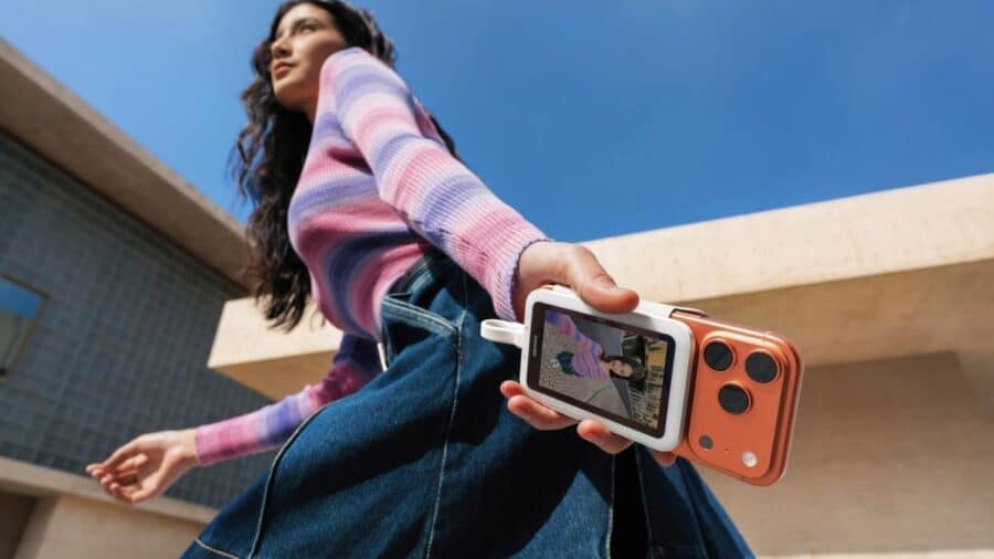 Una ragazza tiene in mano uno smartphone con Insta360 Snap collegato sul retro, usando lo schermo secondario per inquadrarsi all’aperto.