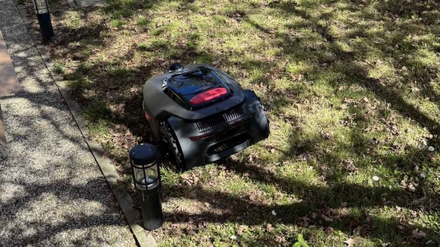 Il MOVA LiDAX Ultra 800 lavora sul prato vicino a una lampada da giardino e al bordo di un vialetto in pietra.