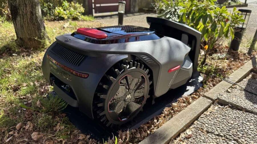 Il robot tagliaerba MOVA LiDAX Ultra 800 è fermo sulla base di ricarica accanto al vialetto, con la grande ruota posteriore tassellata ben visibile.
