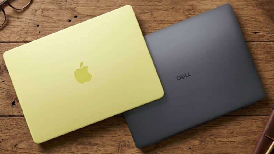 Due laptop chiusi appoggiati su un tavolo in legno: un MacBook Neo giallo in primo piano sovrapposto a un notebook Dell grigio scuro.