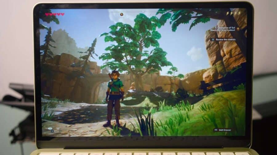 Schermo del MacBook Neo con un videogioco fantasy in esecuzione, mostrando un personaggio in un ambiente naturale con alberi, rocce e interfaccia di gioco visibile.