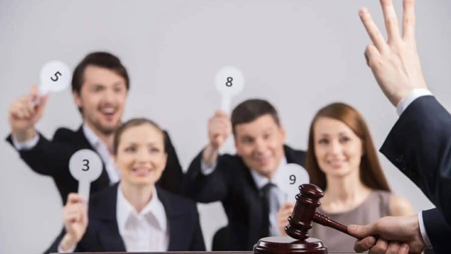 Un banditore impugna il martelletto mentre alcuni partecipanti mostrano palette numerate durante un’asta.
