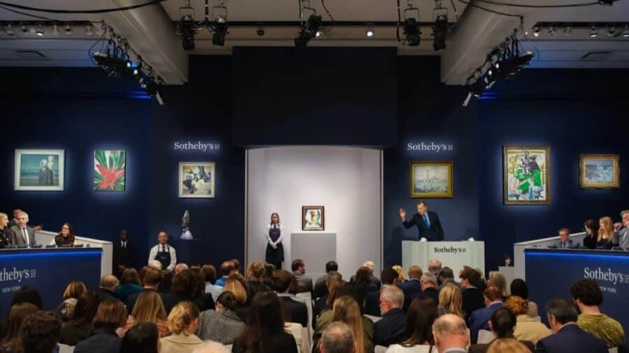 Una casa d’aste Sotheby’s ospita una vendita pubblica con pubblico seduto, opere illuminate e banditore sul palco.
