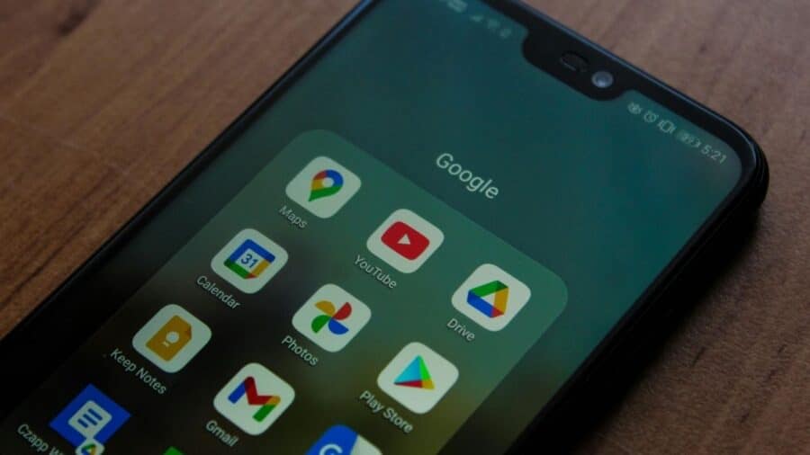 Smartphone Android con cartella Google aperta che mostra le icone delle app Maps, YouTube, Calendar, Photos, Drive, Gmail e Play Store