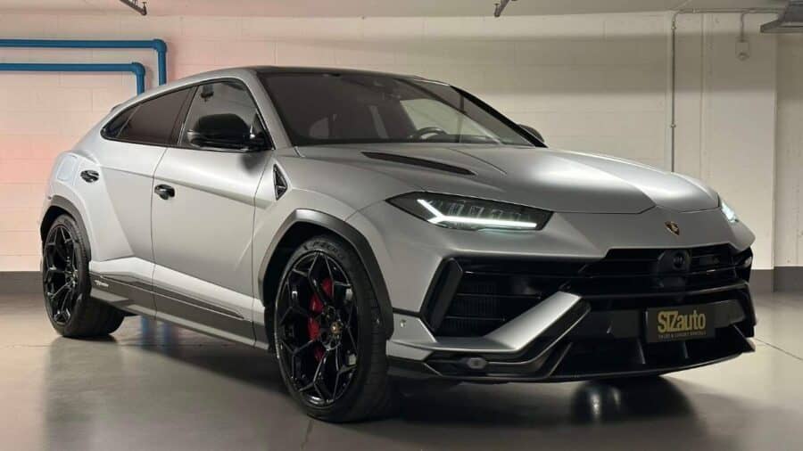 Lamborghini Urus grigia parcheggiata in ambiente interno, ripresa di tre quarti anteriore con paraurti aggressivo e cerchi neri di grande diametro.