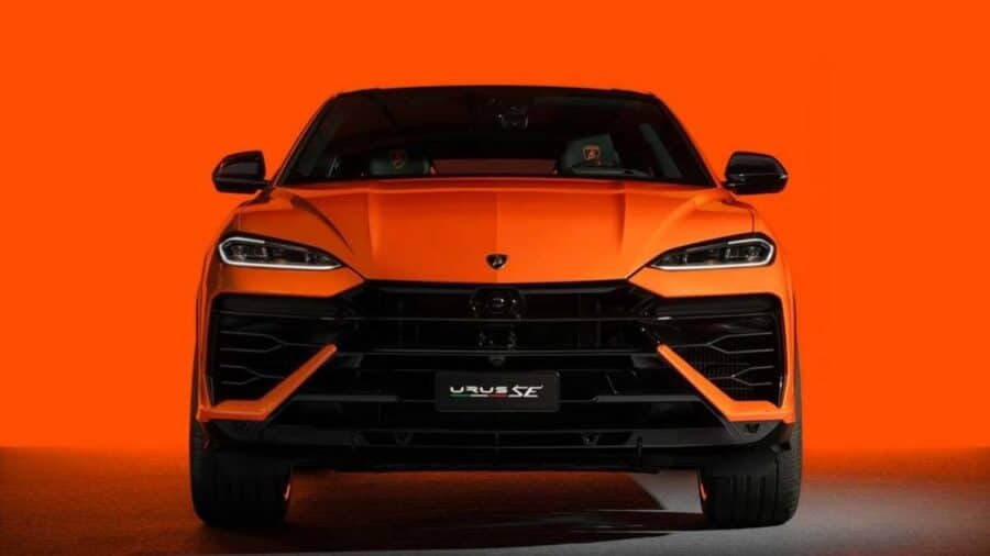 Frontale di Lamborghini Urus arancione su sfondo arancione uniforme, con firma luminosa sottile e grandi prese d’aria nere.