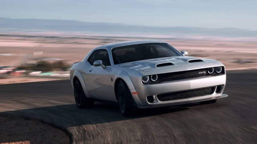 Dodge Challenger SRT Hellcat grigia in movimento su strada aperta, ripresa frontale laterale con cofano bombato e linea da muscle car americana.
