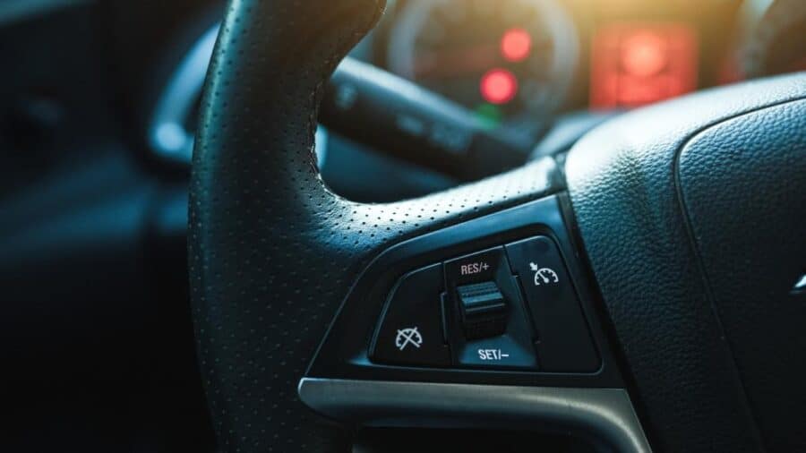 Primo piano dei comandi del cruise control sul volante di un’auto, con tasti per attivazione, ripresa della velocità e regolazione set.