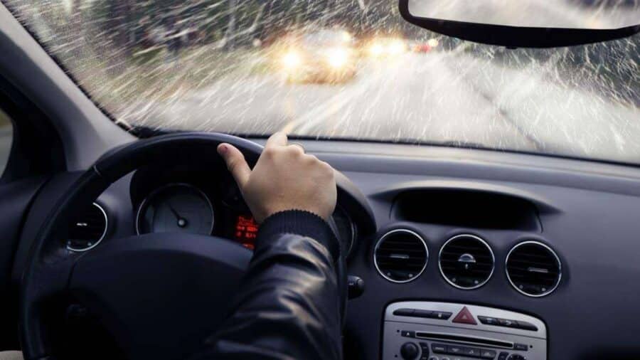 Vista dall’abitacolo di un’auto mentre guida sotto una forte pioggia, con parabrezza bagnato e visibilità ridotta.