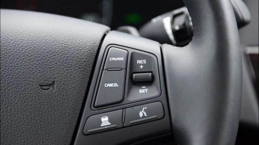 Dettaglio del volante con pulsanti dedicati a cruise control, ripresa velocità, set, assistenza alla distanza e comandi vocali.