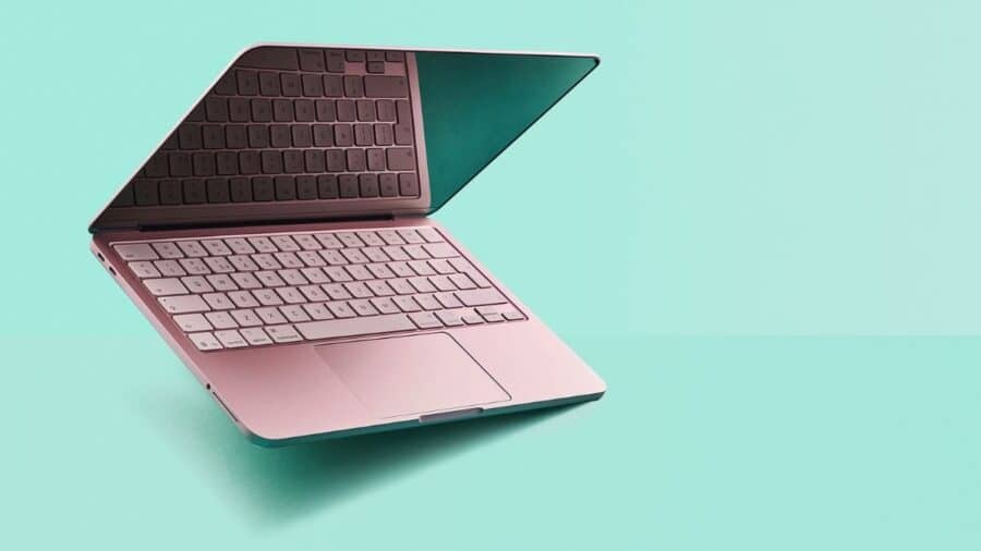 Un MacBook Neo rosa semiaperto è fotografato di profilo su sfondo verde chiaro, con tastiera e trackpad ben visibili.