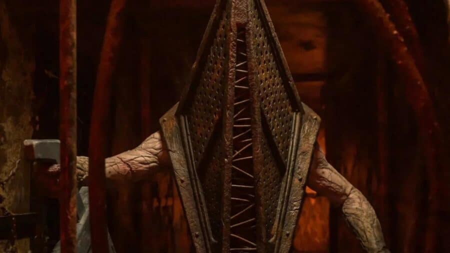 Pyramid Head appare immobile in un corridoio metallico e rossastro, con il caratteristico elmo triangolare che copre interamente il volto.