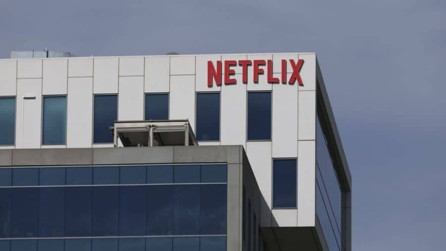 Insegna Netflix rossa sulla facciata di un moderno edificio per uffici con finestre blu e cielo limpido sullo sfondo.