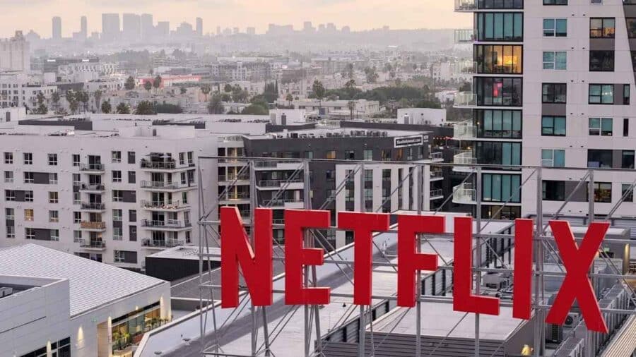 Grande insegna Netflix rossa installata sopra un edificio urbano, con lo skyline cittadino sullo sfondo.