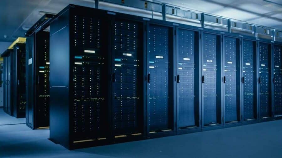 Ampia sala dati con lunghe file di rack server neri allineati, illuminazione fredda e ambiente tipico di un moderno supercomputer center.