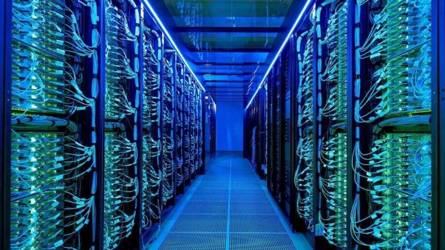 Corridoio interno di un data center ad alta densità con rack pieni di cavi, led blu e infrastruttura di rete avanzata su entrambi i lati.