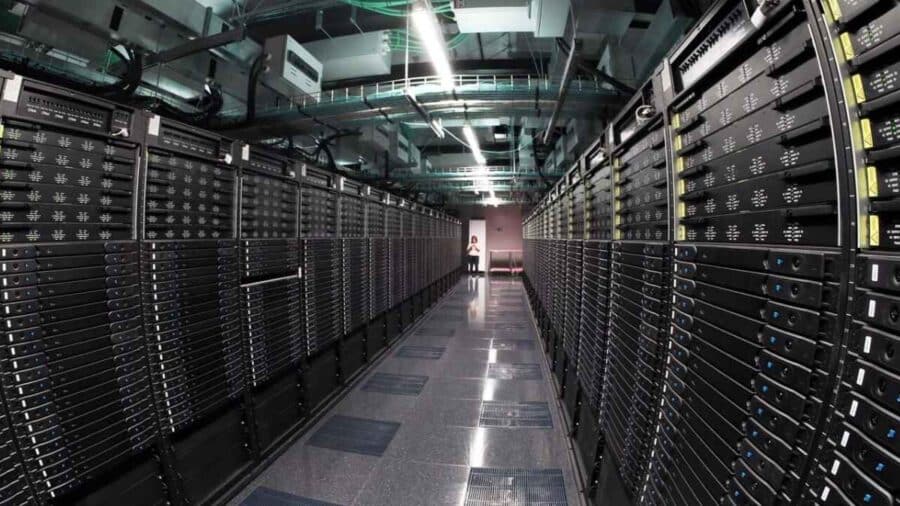 Lungo corridoio di un centro di calcolo con file di armadi server industriali neri e una persona visibile in fondo alla sala.