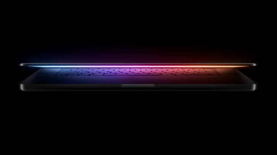 Profilo laterale di un laptop Apple molto sottile, semiaperto nel buio, con tastiera illuminata da una sfumatura blu e rossa.
