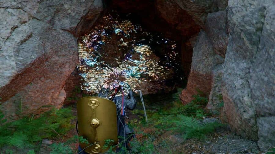 Il protagonista di Crimson Desert affronta l’ingresso di una grotta mentre un muro di bismuto brillante esplode in scintille luminose dopo essere stato colpito con un attacco a distanza.
