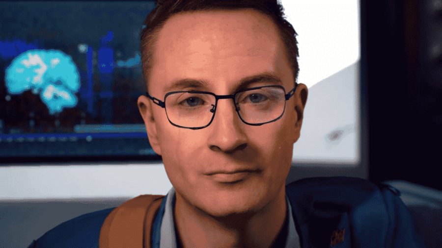 Primo piano di Heartman in Death Stranding, personaggio interpretato da Nicolas Winding Refn, con occhiali e sfondo tecnologico.