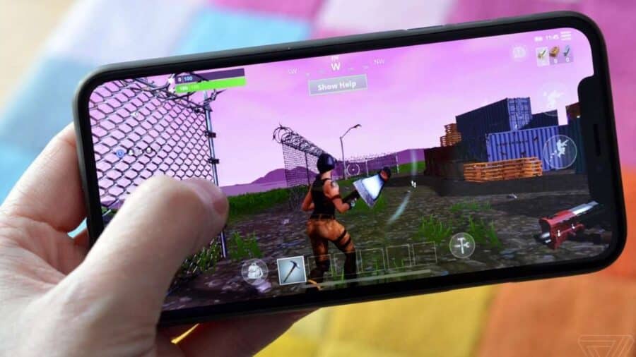 Persona che tiene in mano un iPhone in orizzontale mentre gioca a Fortnite, con il personaggio visibile sullo schermo in una partita mobile.