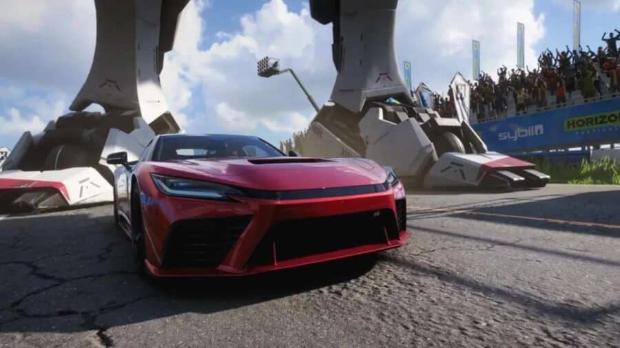 Coupé rossa parcheggiata davanti a una gigantesca struttura meccanica durante un evento del festival, con folla sugli spalti.