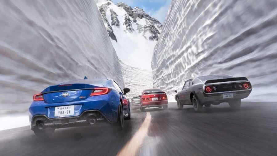 Gruppo di auto sportive corre in un corridoio scavato nella neve tra alte pareti bianche, con strada ghiacciata e montagne sullo sfondo.