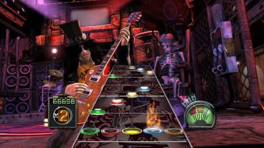 Schermata gameplay di Guitar Hero con note colorate in scorrimento, chitarra elettrica in primo piano e scenario da concerto rock.