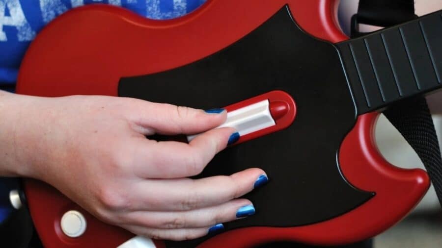 Primo piano di una chitarra controller rossa in plastica, con mano sul selettore usato nei rhythm game musicali.