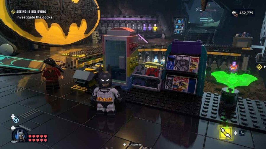 Batman nella Batcaverna di LEGO Batman L’Eredità del Cavaliere Oscuro, circondato da gadget, monitor, costumi e oggetti collezionabili.