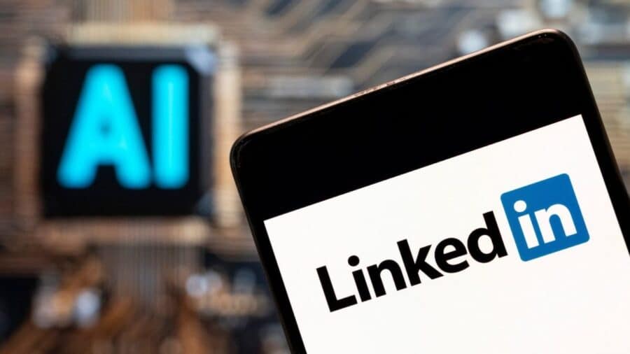 Primo piano di uno smartphone con il logo LinkedIn sullo schermo, con una scritta luminosa “AI” sfocata sullo sfondo.