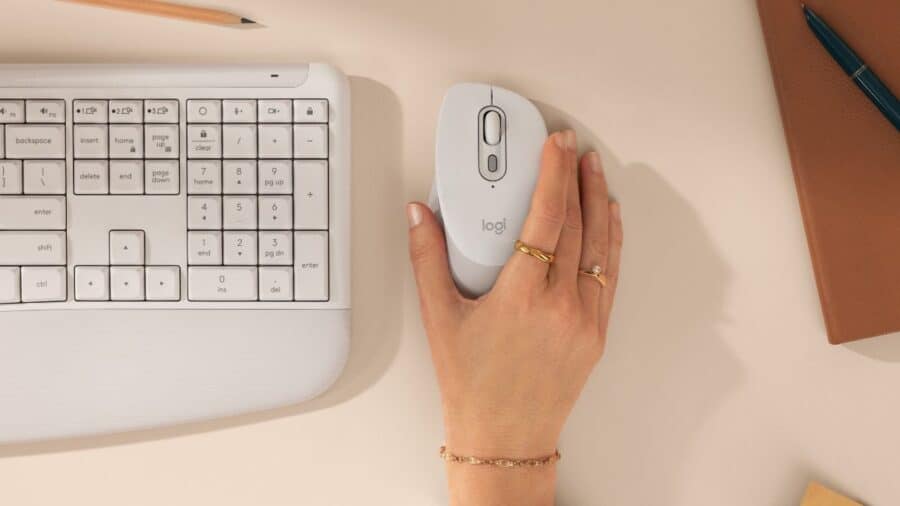 Vista dall'alto di mano che impugna il mouse Logitech M840 L bianco accanto alla tastiera MK880