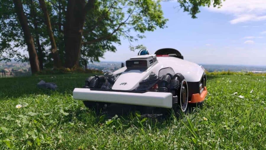 Mammotion Luba 3 AWD 3000 su prato in pendenza con panorama collinare, vista laterale che mostra il sistema di trazione e la scocca bianca con dettagli arancioni
