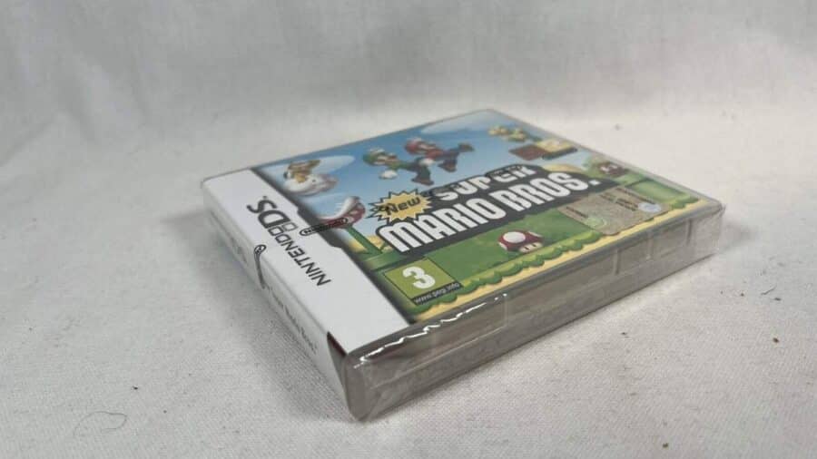 Confezione sigillata di New Super Mario Bros. per Nintendo DS appoggiata su una superficie chiara, fotografata in prospettiva laterale.