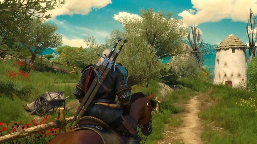 Geralt di Rivia a cavallo in The Witcher 3, mentre attraversa un sentiero di campagna tra ulivi, fiori e mulini a vento.