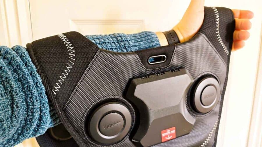 Persona che tiene in mano il Woojer Haptic Vest 4 mostrando il retro del gilet con due trasduttori circolari e il modulo centrale.
