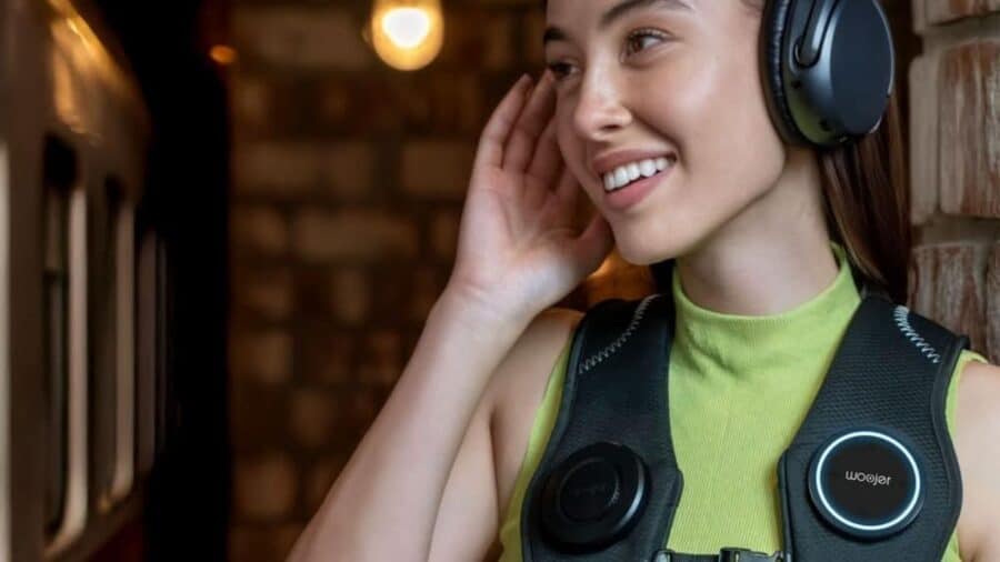 Donna che indossa il Woojer Haptic Vest 4 insieme a cuffie over-ear, sorridendo mentre ascolta contenuti audio in un ambiente interno.