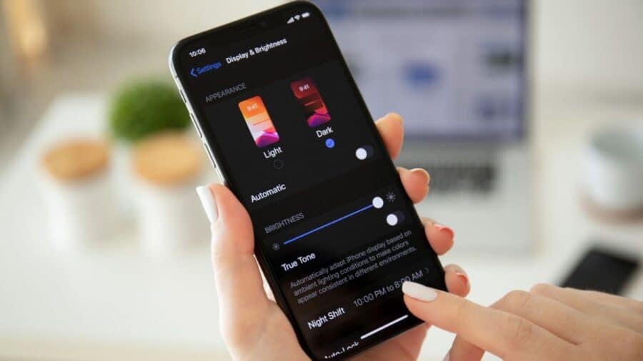 Persona che usa un iPhone nella schermata “Display & Brightness”, con la modalità Dark selezionata e le opzioni di luminosità visibili sul display.